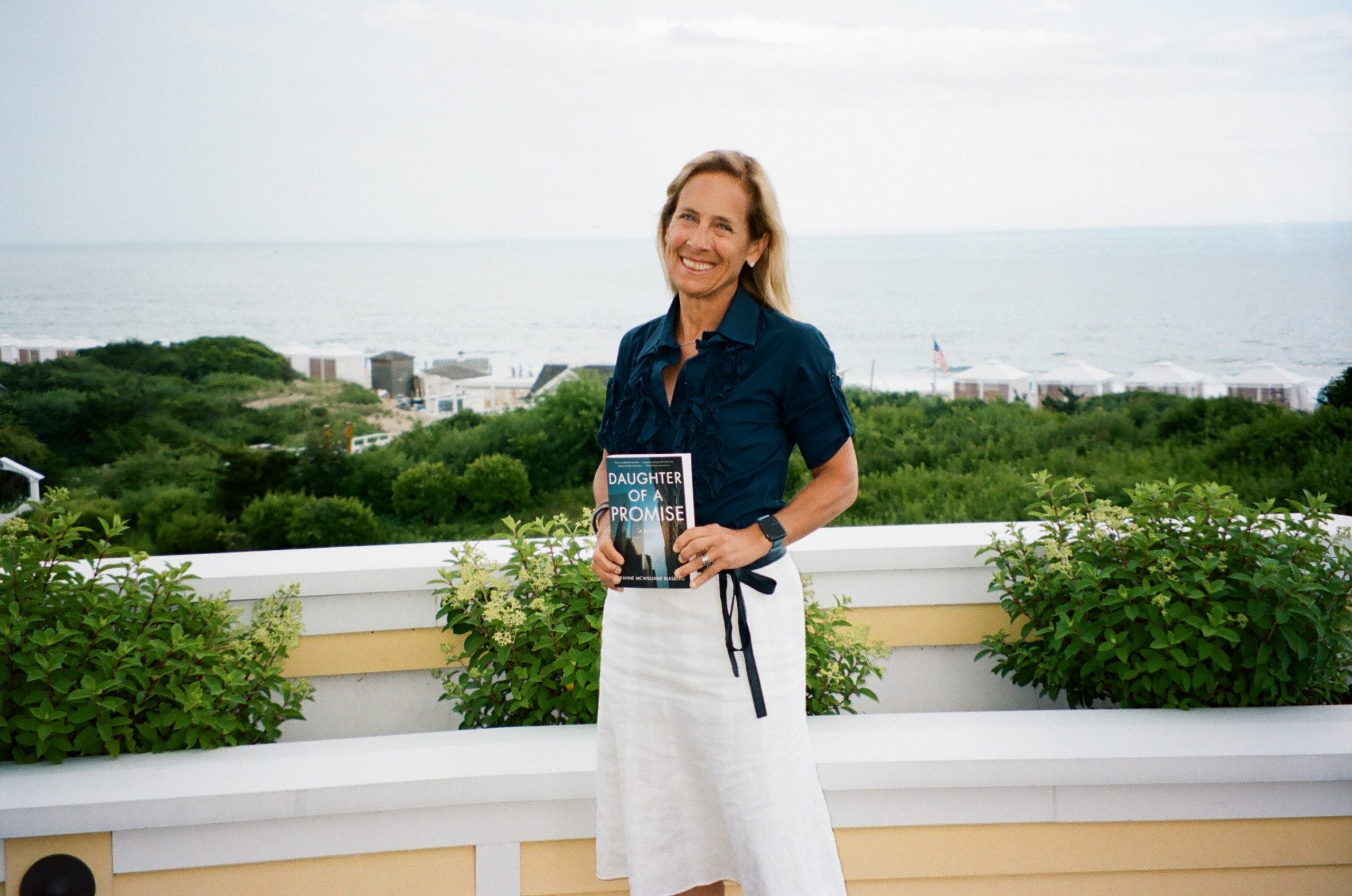 jeanne-blasberg-holding-book-daughter-of-a-promise-in-westerly-rhode-island--inspiration-for-long-harbor-in-front-of-the-ocean